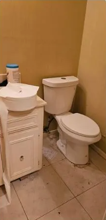 Bathroom with a toilet and sink cabinet. Dirty tile floor and yellow walls.
