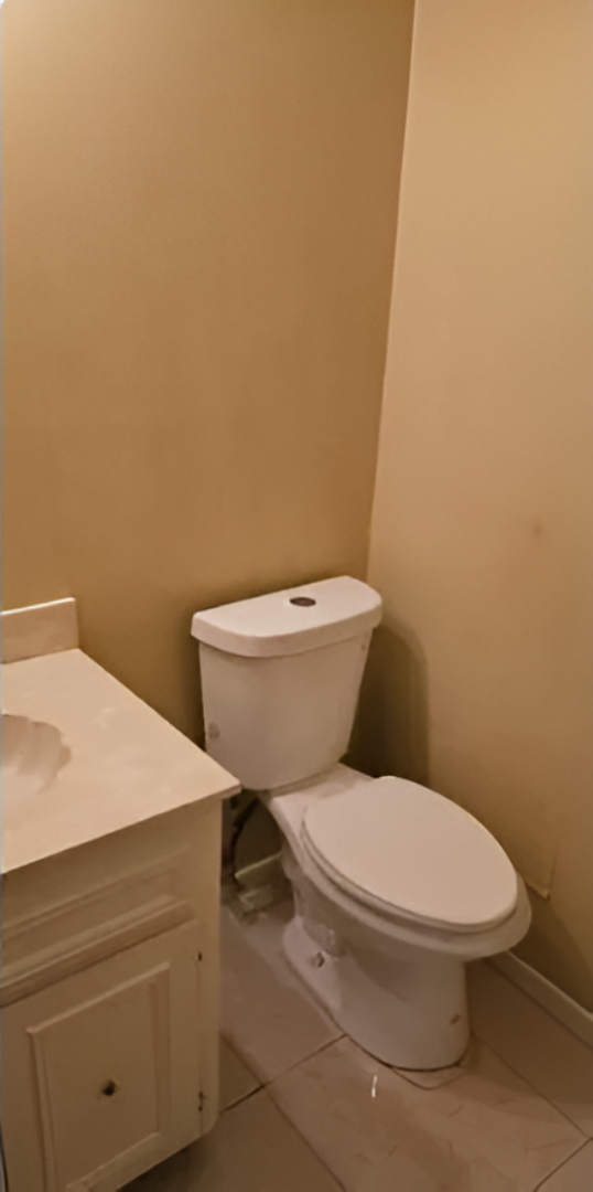 A small bathroom with a white toilet and a beige cabinet. Beige walls and floor.