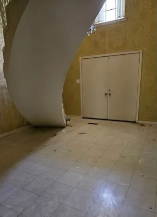 Interior with damaged ceiling. White doors, tiled floor, and gold-toned walls in a room.