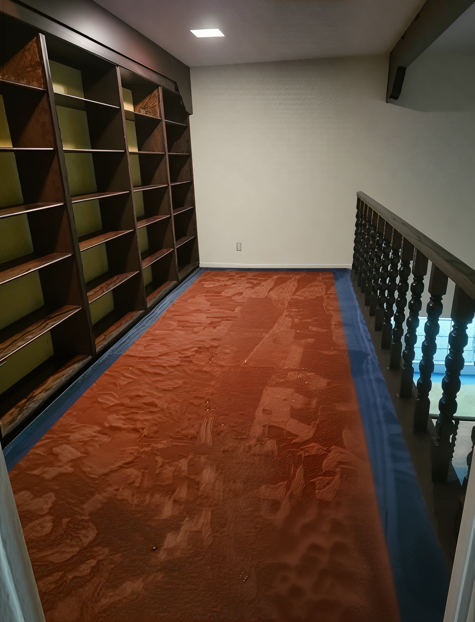 Empty library loft with dark wood bookshelves, rust-colored rug, blue carpet border, and wooden railing.