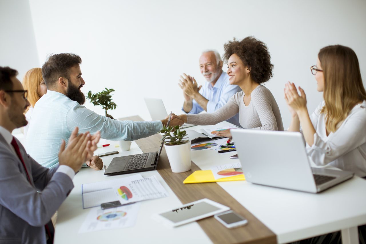 A group of people are sitting around a table with laptops and applauding.