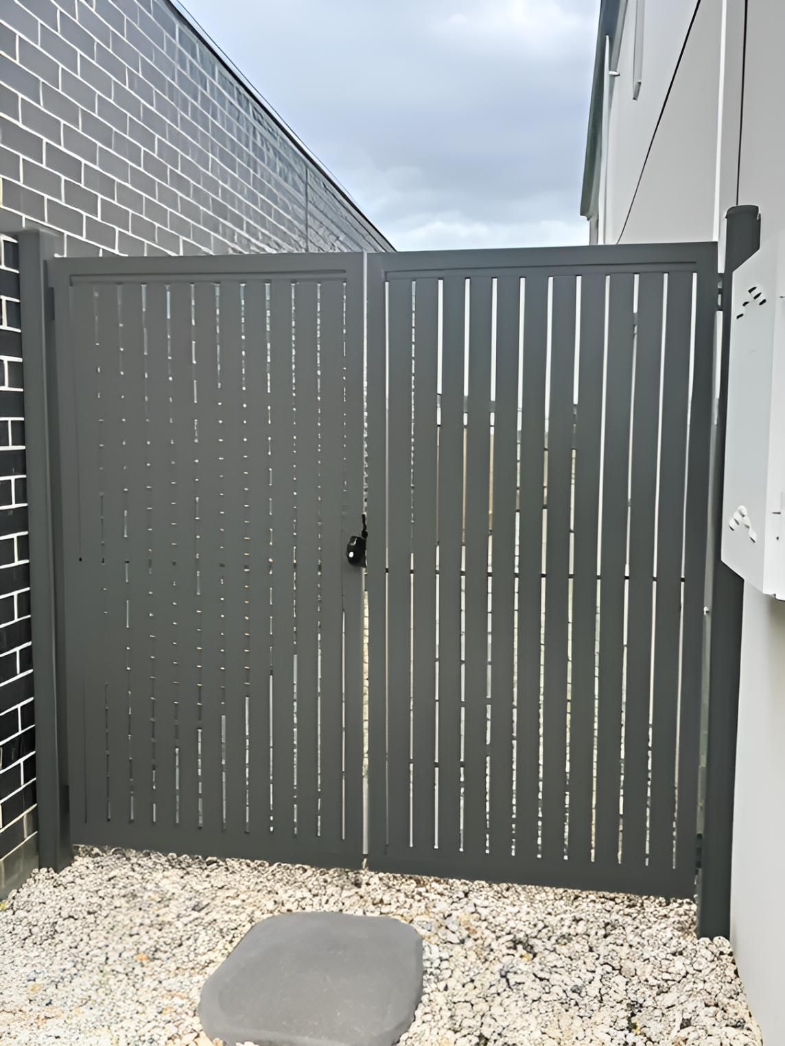 A Gray Gate Is Sitting In Front Of A Brick Building — Talking Fences In Portarlington, VIC