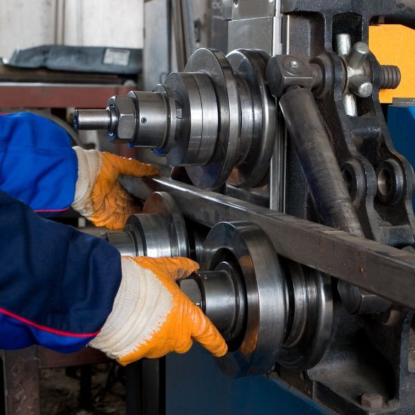 Worker in blue uniform and orange gloves operating a metal rolling machine.