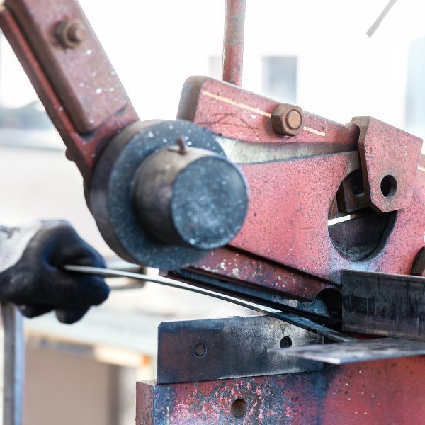 Close-up of person's hand in glove using a metal shear to cut metal rods. Red metal machine.