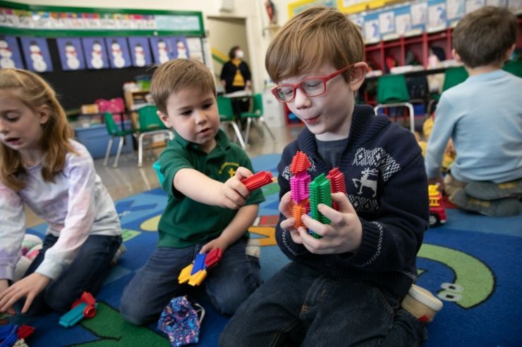A group of children are playing with toys on the floor in a classroom.