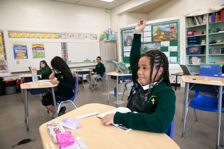 A young girl is raising her hand in a classroom.