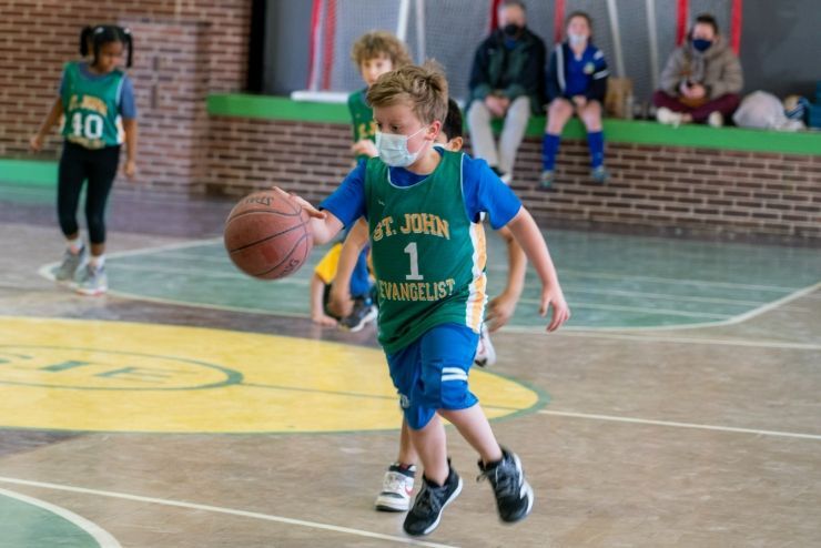 A young boy wearing a mask is dribbling a basketball on a court.