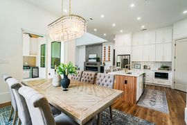 Bright modern kitchen and dining area with white cabinets, wood accents, and a large table under a chandelier