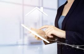 Person using a tablet with a glowing house icon in a bright office setting