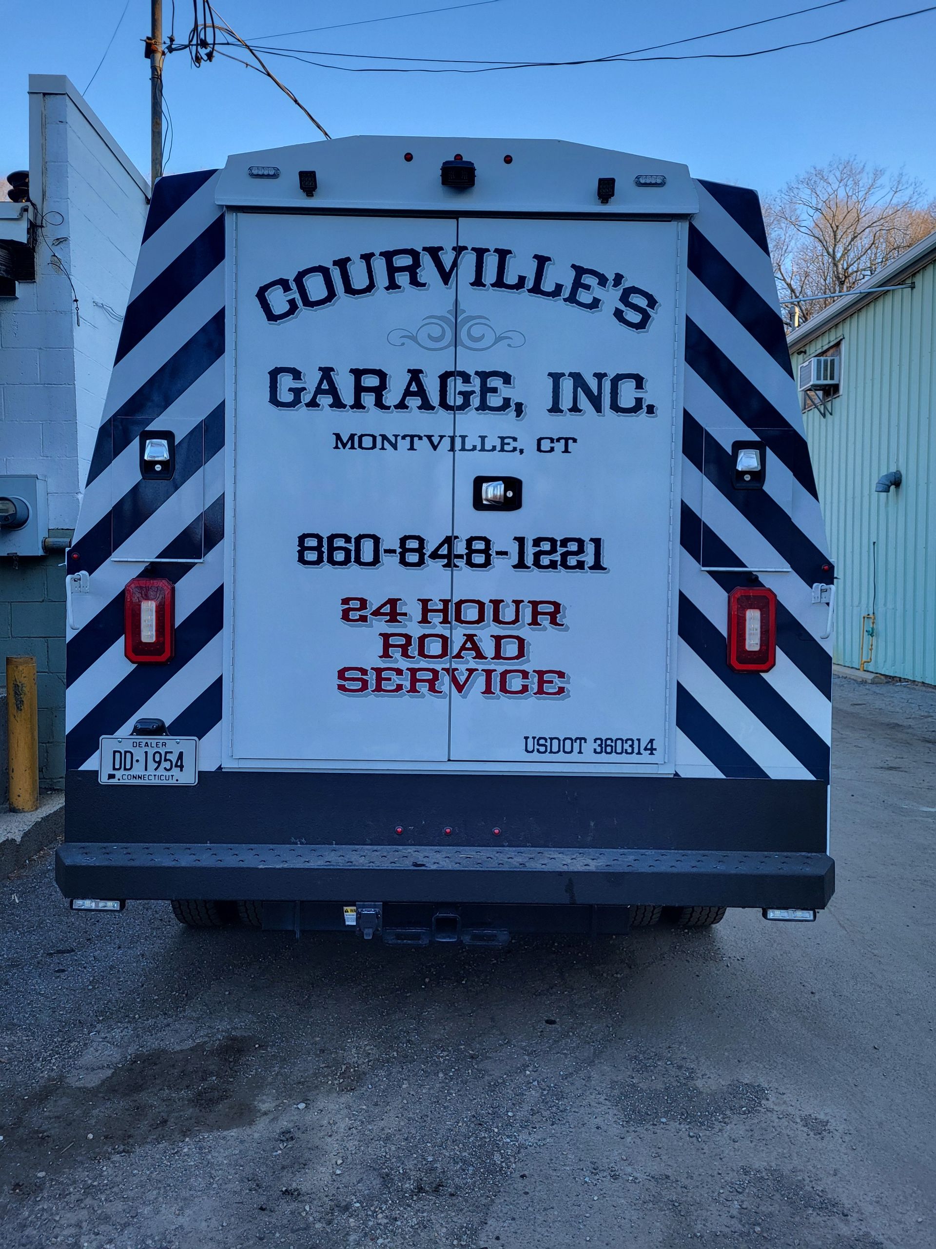 Rear view of Courville's Garage, Inc. tow truck with service information and phone number, against a blue sky.