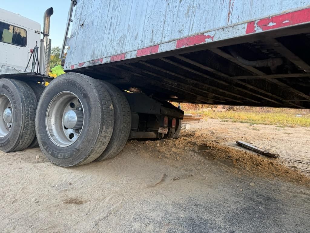 Semi-truck trailer, bottom view, on dirt, with wheels and undercarriage.