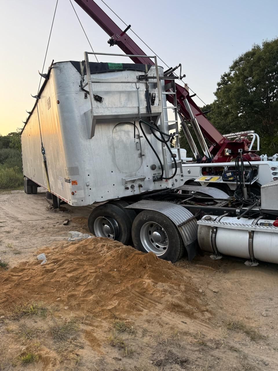A tow truck is pulling a large semi-trailer out of the dirt.