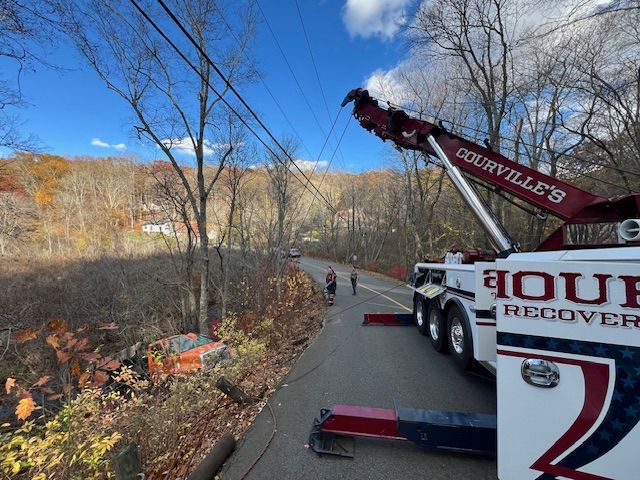 Tow truck near power lines and roadside trees on a sunny day. Two figures walk on road.
