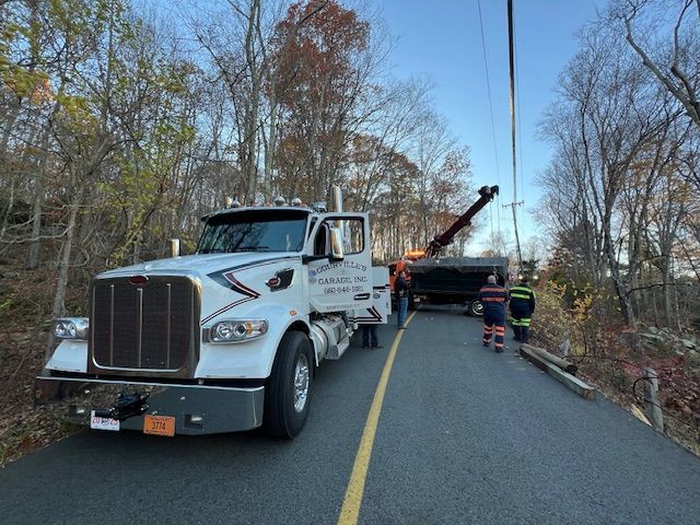 Tow truck pulling a vehicle from a road; trees line the sides.