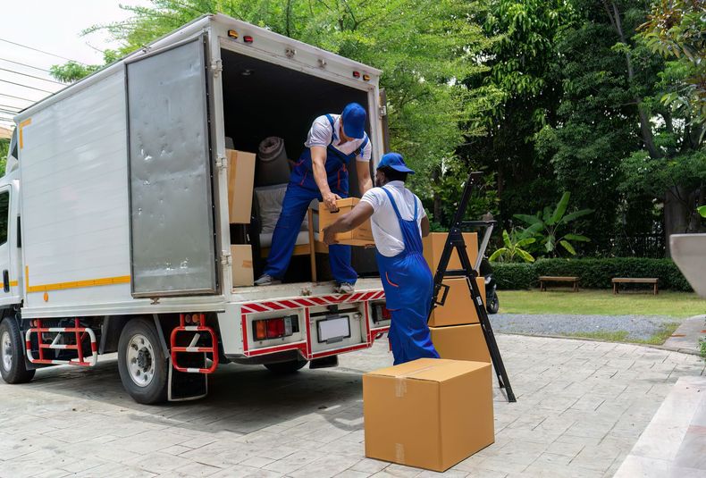 Workers unloading boxes from a white truck in a park-like area