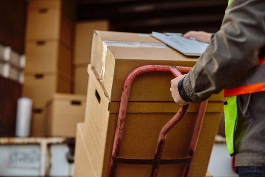 Worker moving stacked cardboard boxes with a hand truck in a warehouse