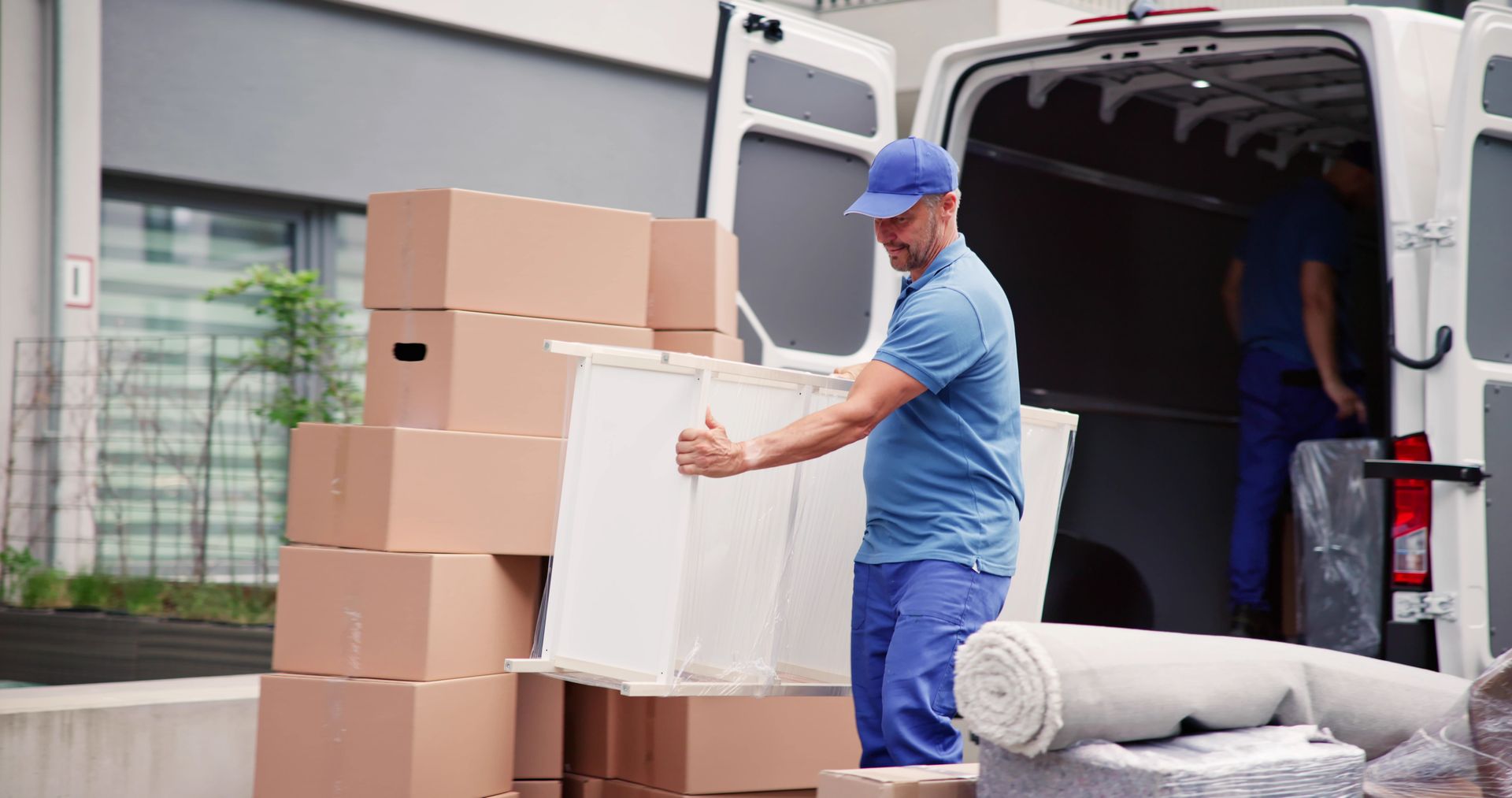 Mover loading a white box from stacked cardboard boxes into a white delivery van
