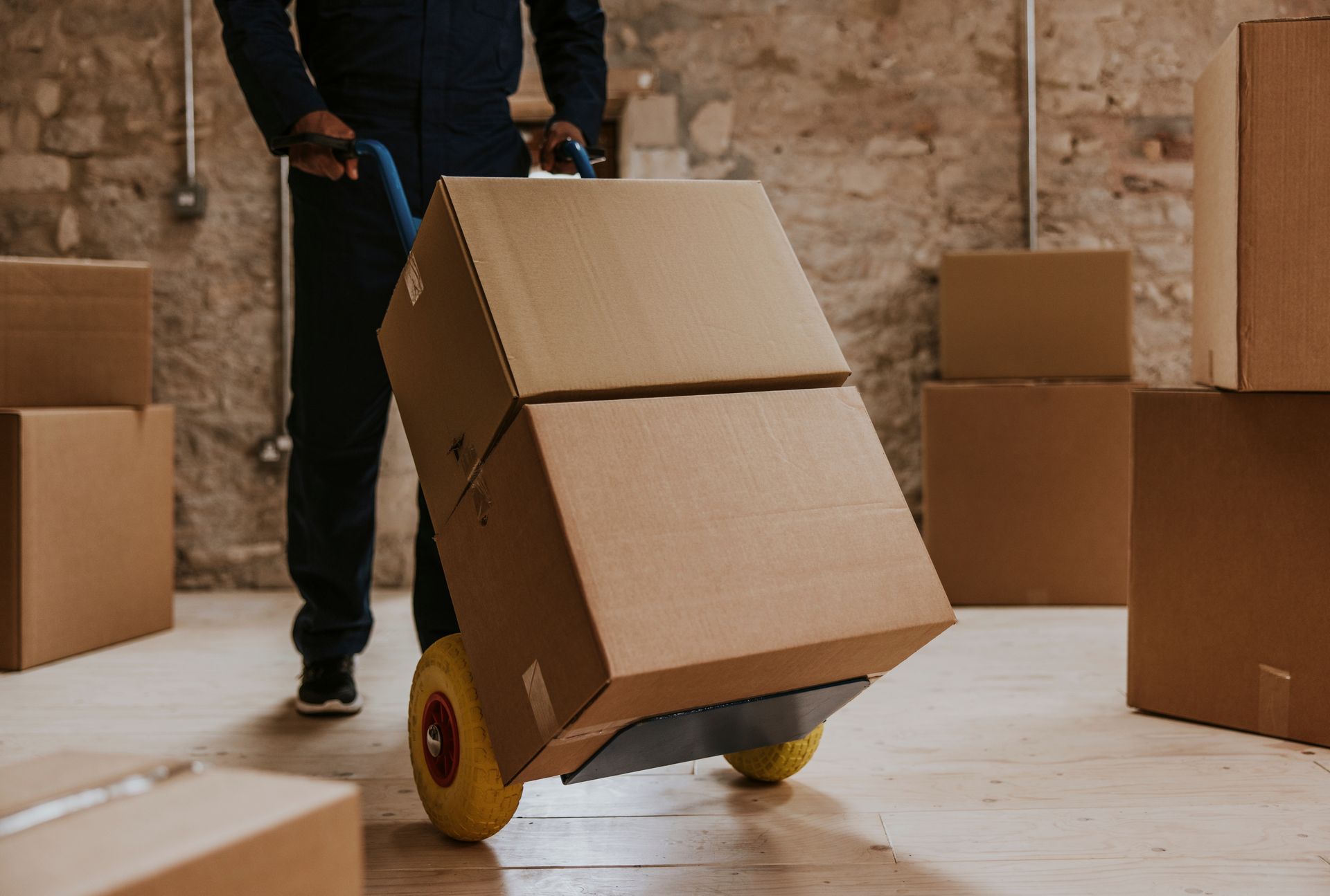Person moving a large cardboard box on a hand truck in a warehouse or storage room.