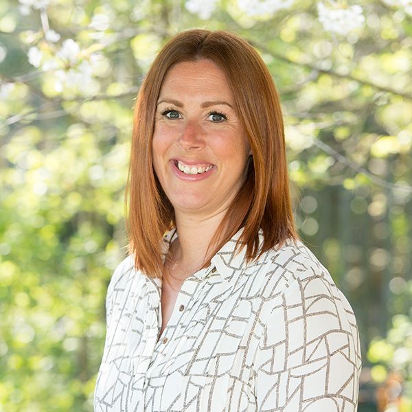 A woman with red hair is wearing a white shirt and smiling.
