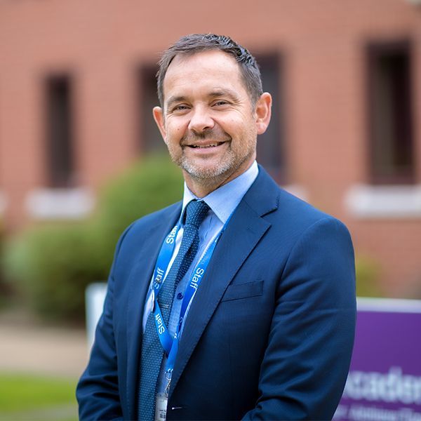 A man in a suit and tie is smiling in front of a building.