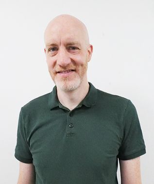 A bald man with a beard is wearing a green polo shirt and smiling.