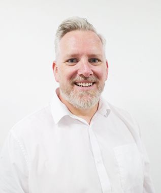 A man with a beard is wearing a white shirt and smiling.