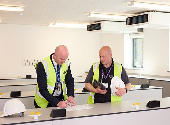 Two men in yellow vests are standing next to each other in a room.