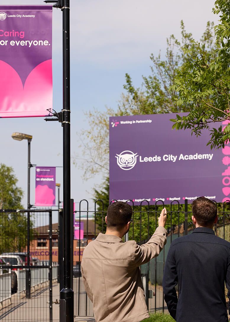 Two men are standing in front of a sign that says leeds city academy