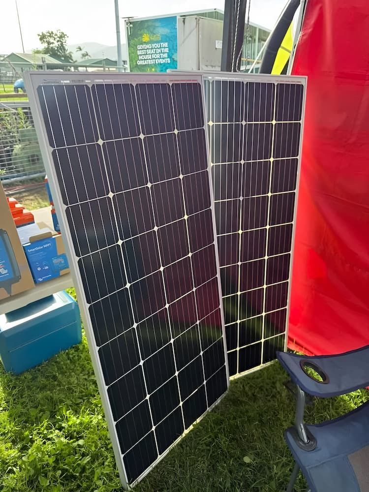 Two Solar Panels Leaning Against a Red Backdrop on Grass, a Blue Box — Edmonton Battery Centre in Bentley Park, QLD