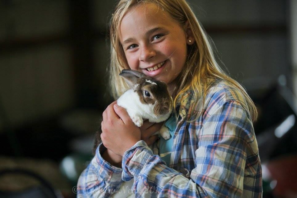 A smiling person with long blonde hair holds a small, brown and white rabbit in their arms.