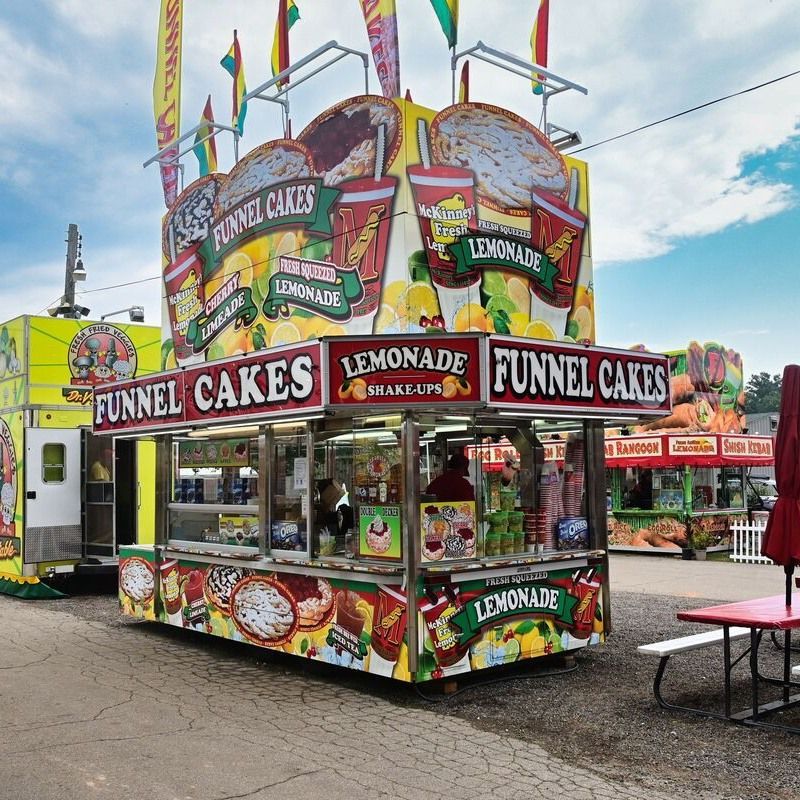 A colorful carnival concession stand brightly decorated with graphics of funnel cakes and lemonade at an outdoor fair.