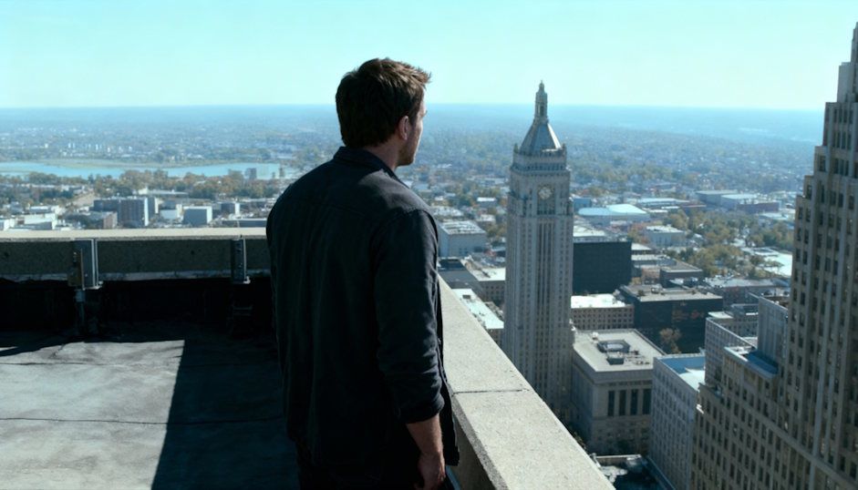 Man standing next to the edge of a skyscraper staring off the top of the building in fear of heights in downtown Cleveland 
