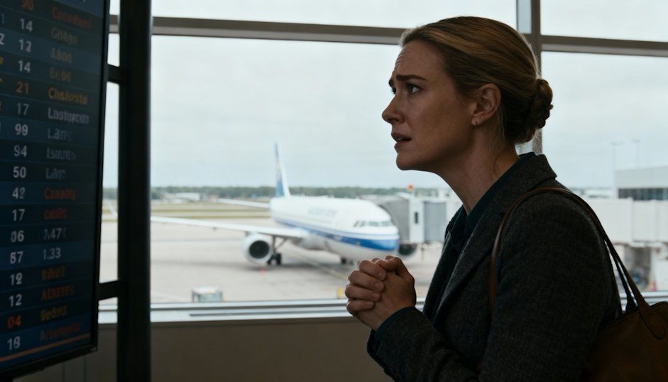 Woman staring anxiously at a flight departure sign inside at Cleveland Hopkins Airport looking at a plane out the window with a fear of flying