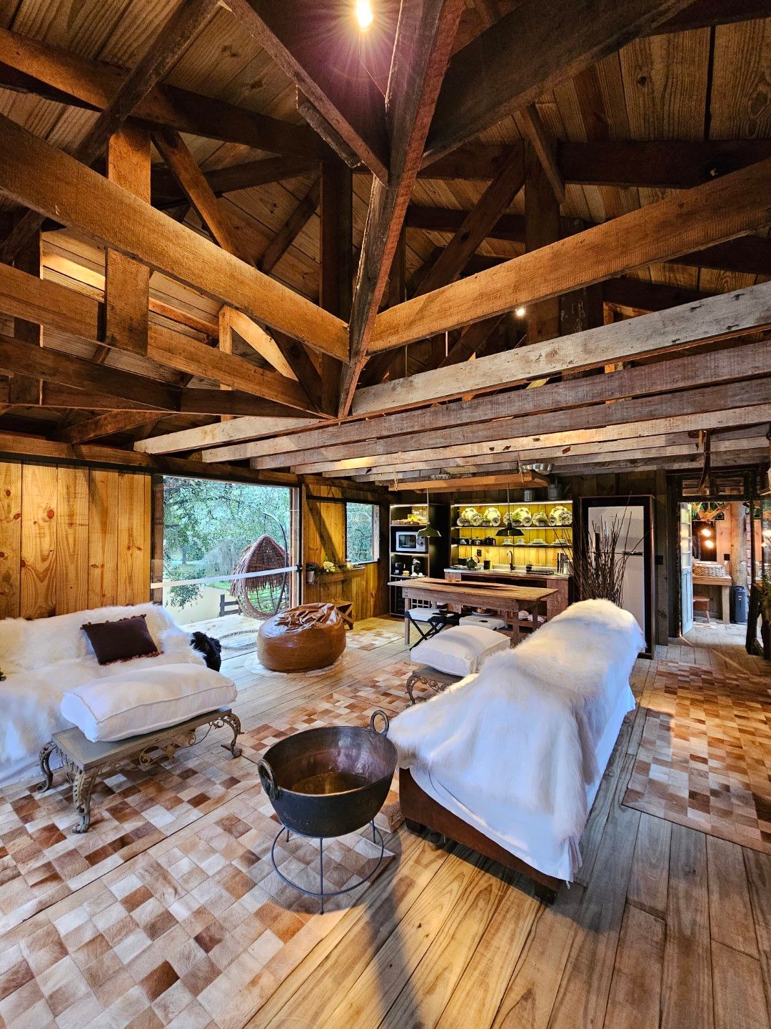 Interior aconchegante de cabana de madeira com assentos, lareira e bar. Janelas amplas com vista para a natureza.