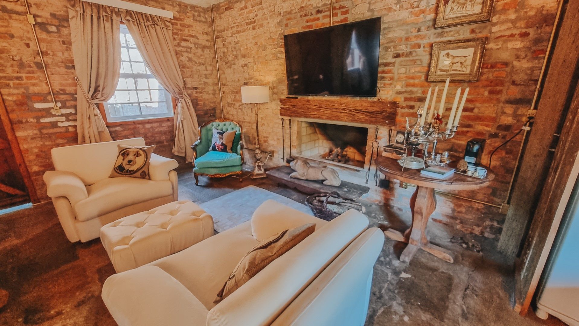 Sala de estar aconchegante com paredes de tijolos, lareira, sofás brancos e uma poltrona azul-petróleo.