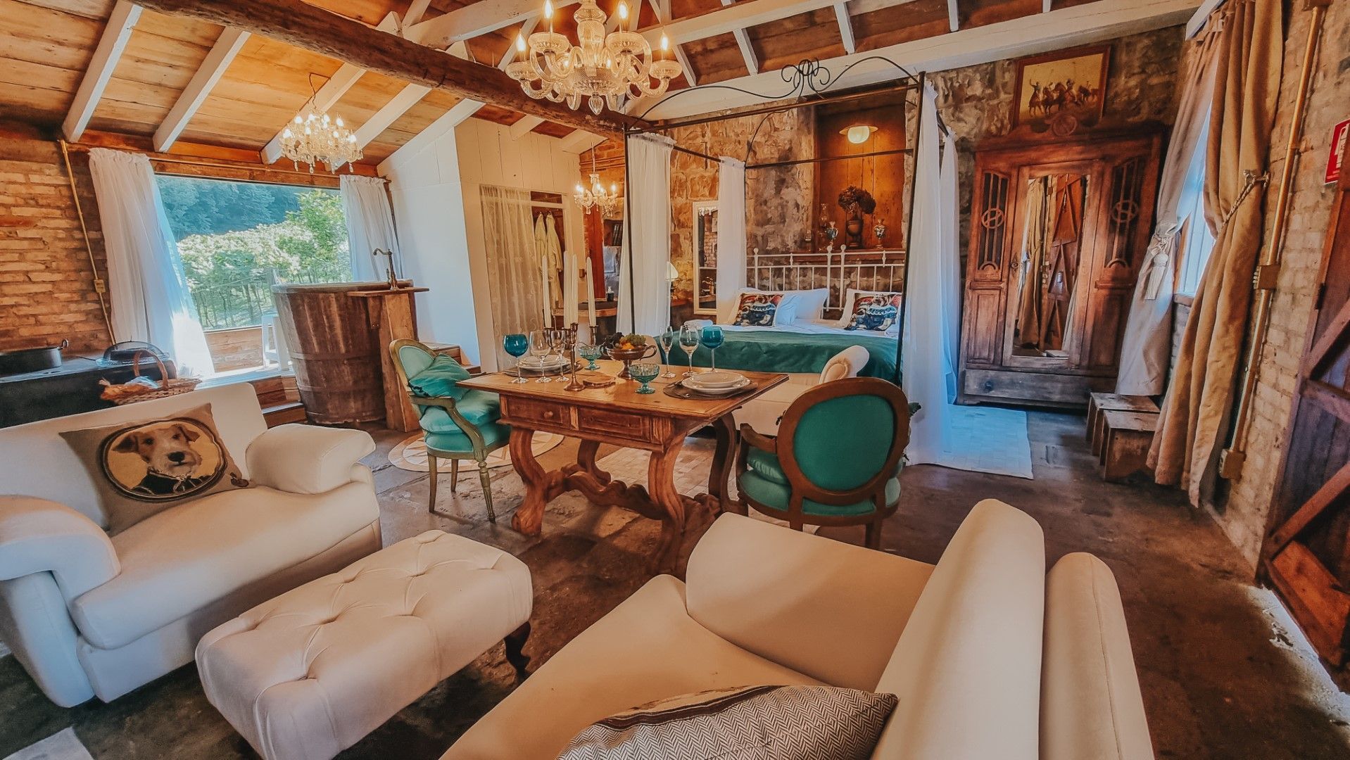 Sala de estar aconchegante com sofás brancos, mesa ornamentada e lustre; detalhes em tijolo e madeira.