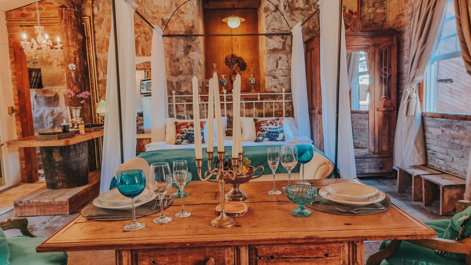 Quarto aconchegante com cama de dossel, velas acesas e mesa posta para o jantar. Paredes rústicas de pedra.