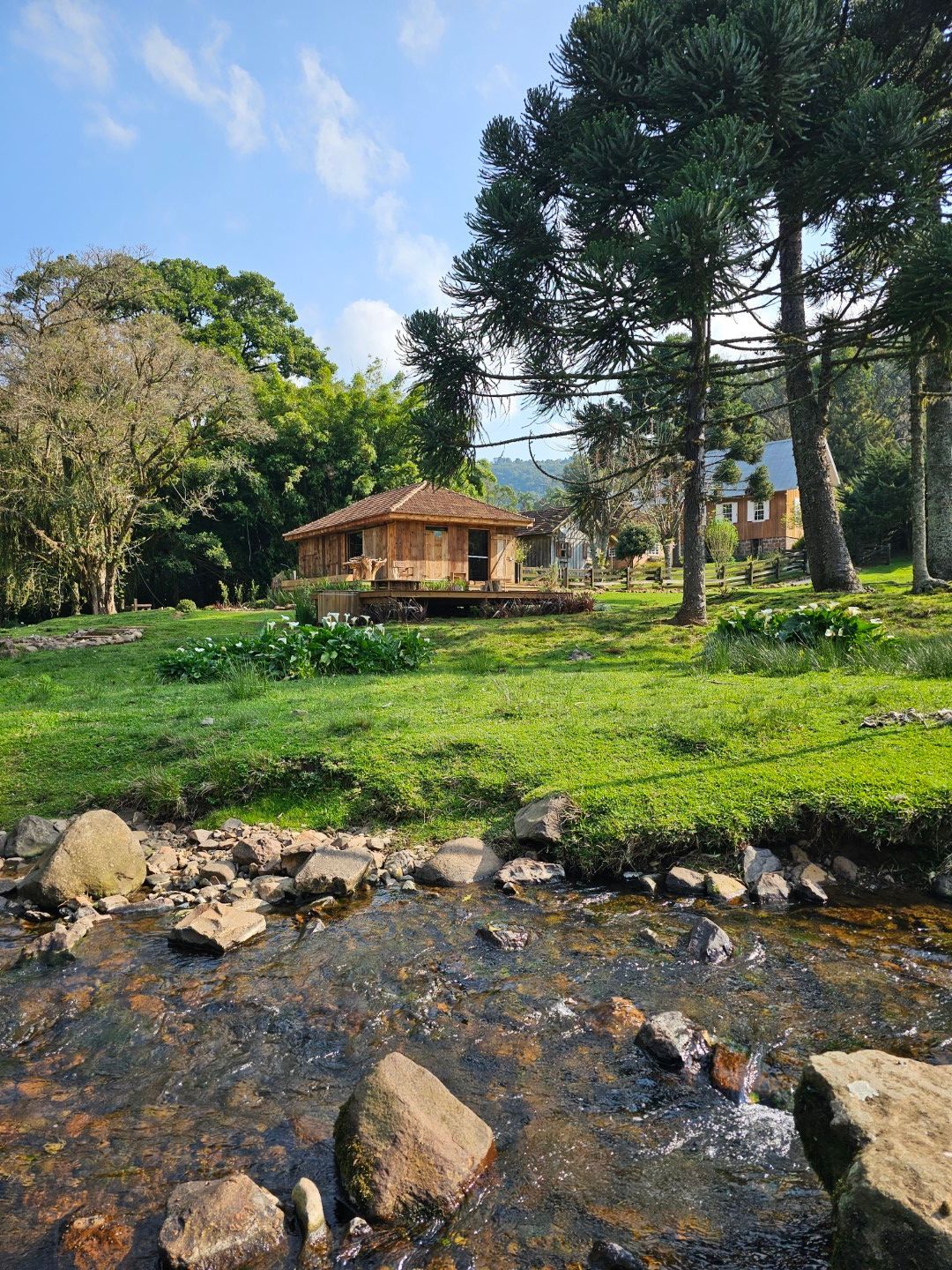 Casa de madeira com gramado verde, construção de tijolos, cadeiras e céu nublado.