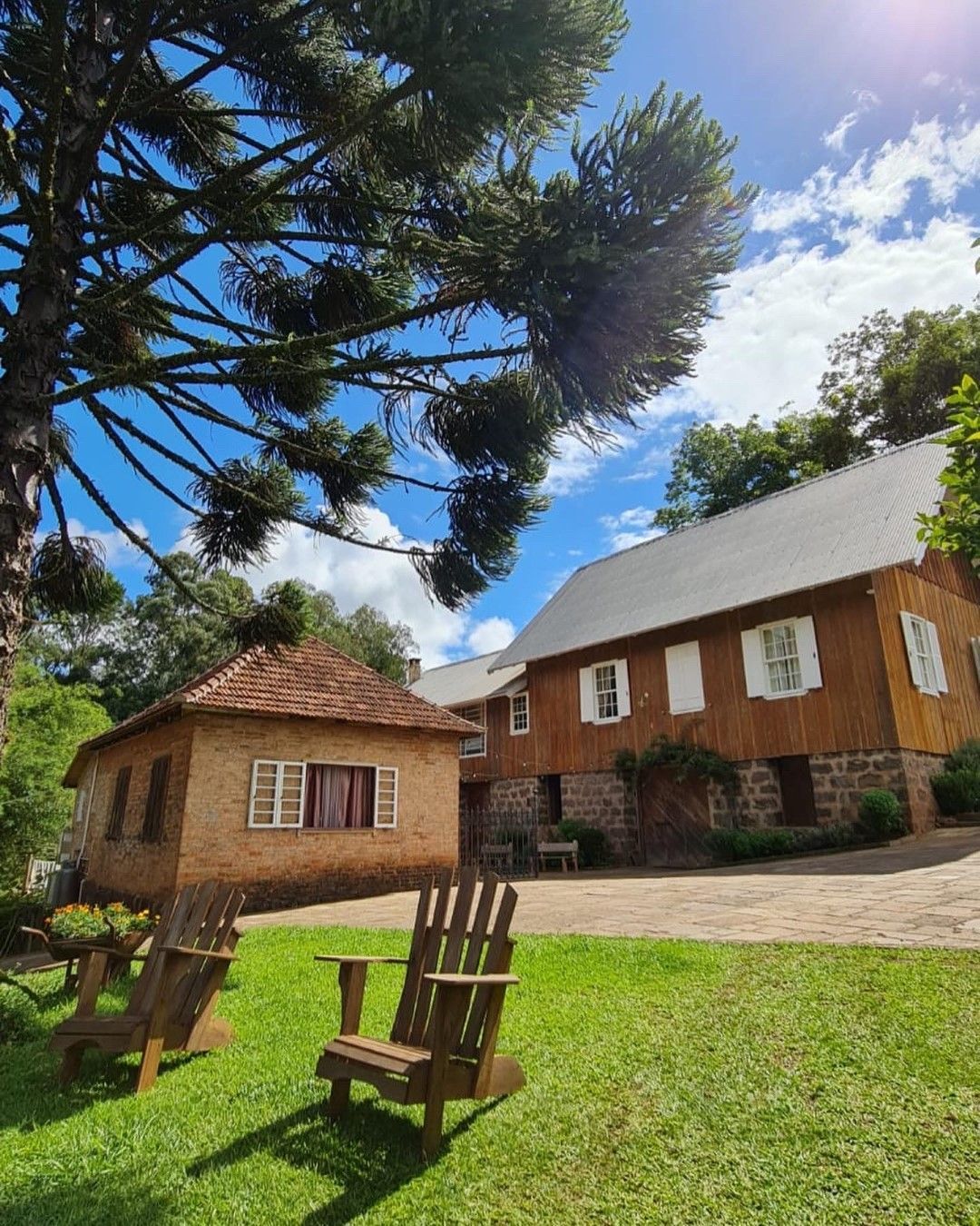 Cadeiras de madeira em um gramado em frente a um prédio rústico com uma dependência de tijolos marrons.