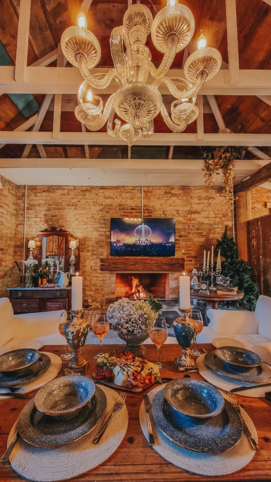 Conjunto formal de mesa de jantar para uma refeição com lareira e lustre em uma sala de jantar rústica.