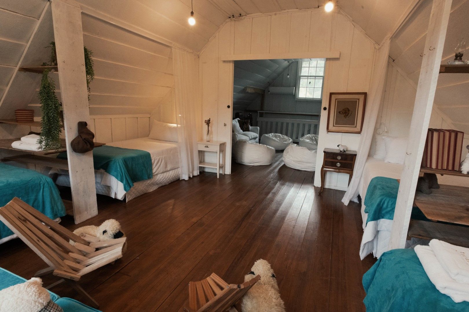 Quarto aconchegante e rústico com camas, piso de madeira e uma porta aberta para uma área de estar.