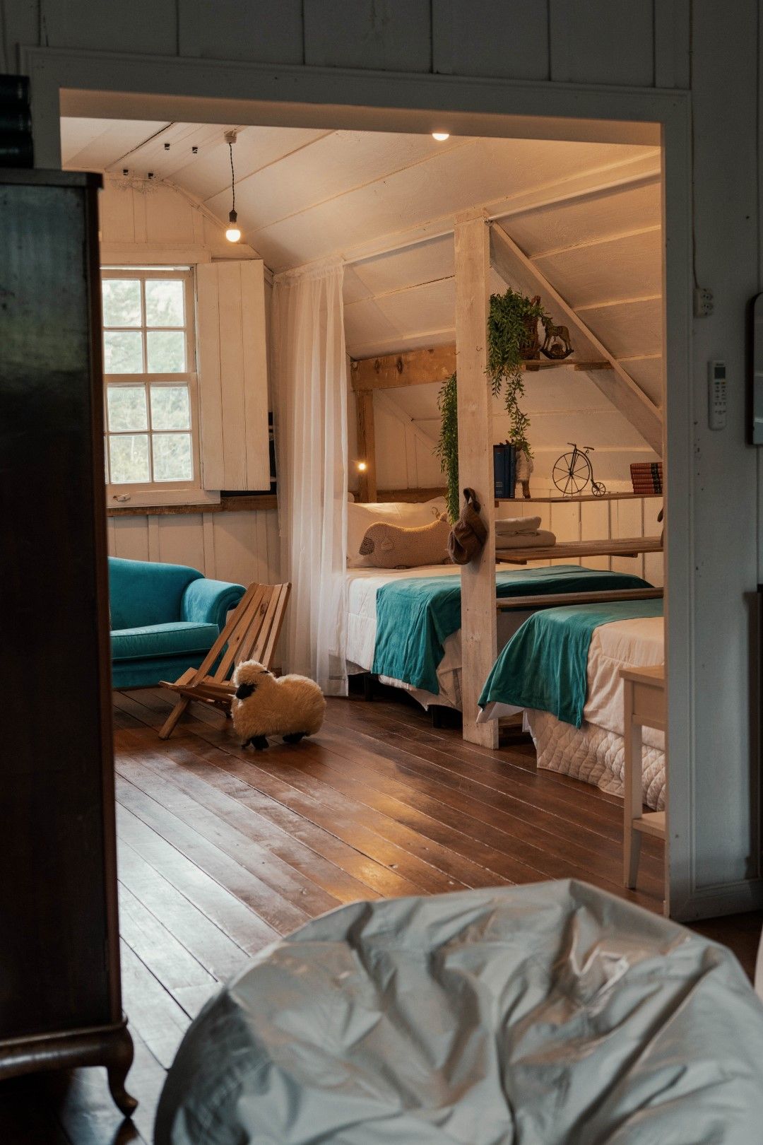 Interior aconchegante da cabine: sofá azul-petróleo, duas camas com cobertores turquesa, escultura de ovelha, piso de madeira.
