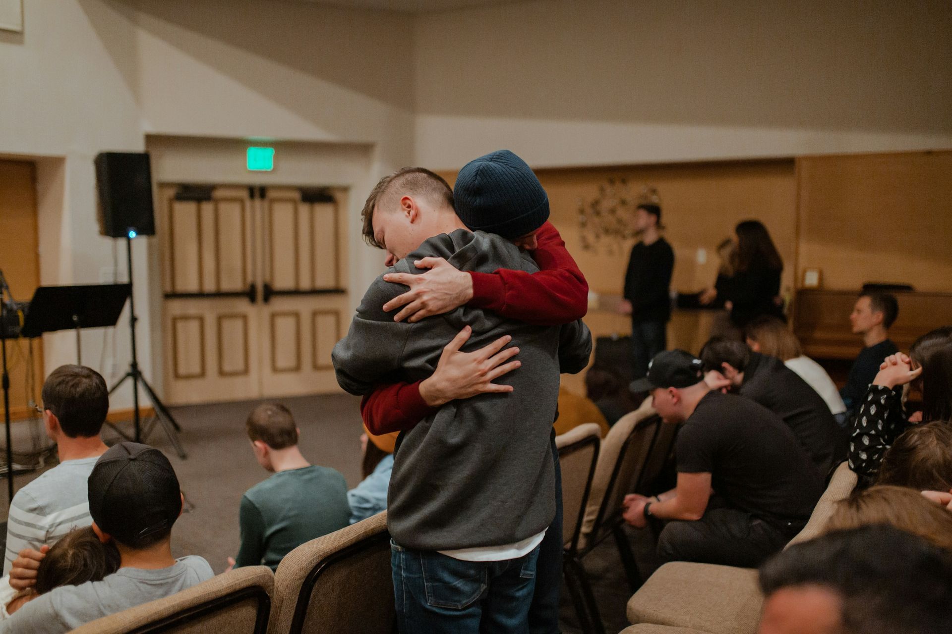 People hugging in front of an audience in a dim room.