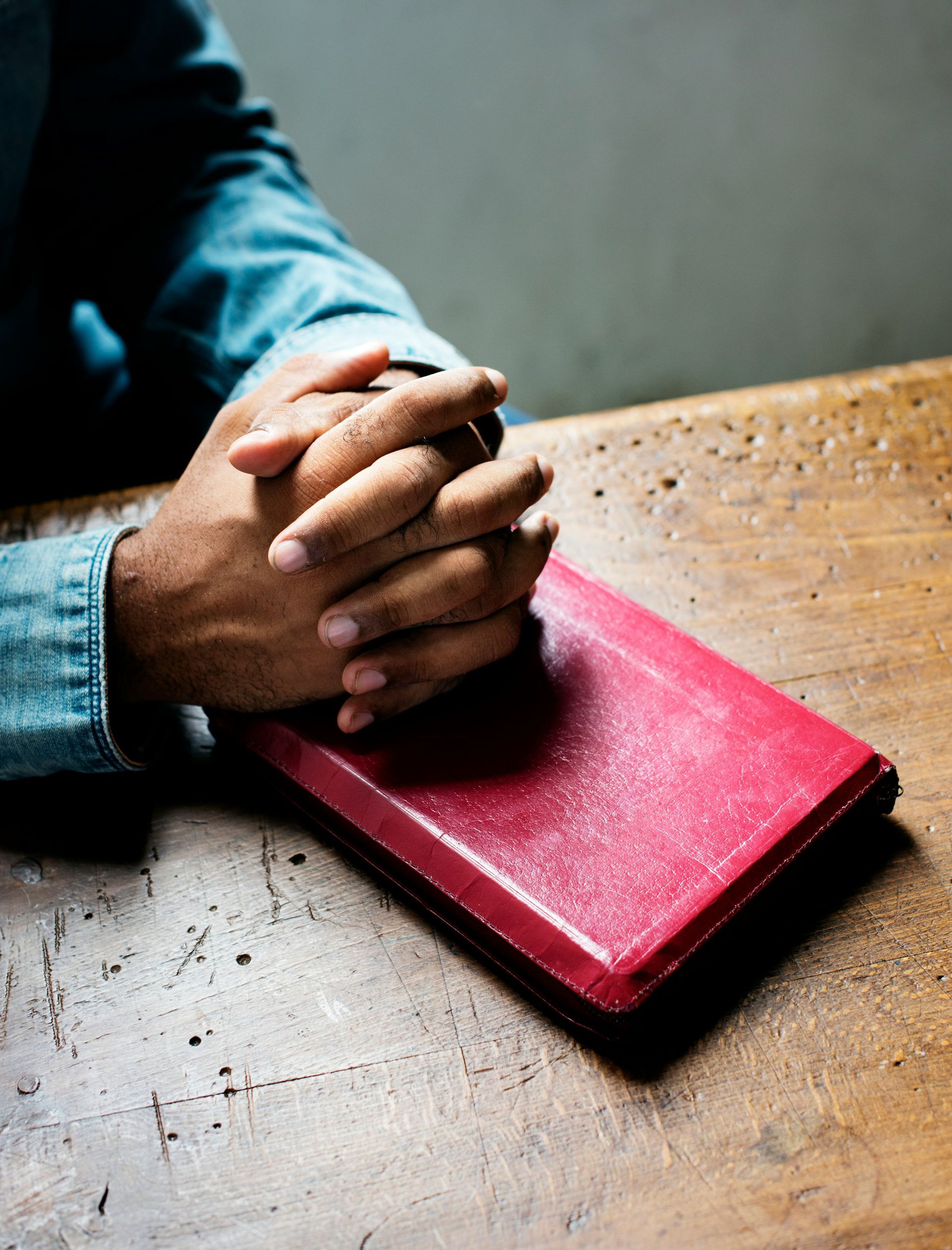 Hands clasped on a red book on a wooden surface.
