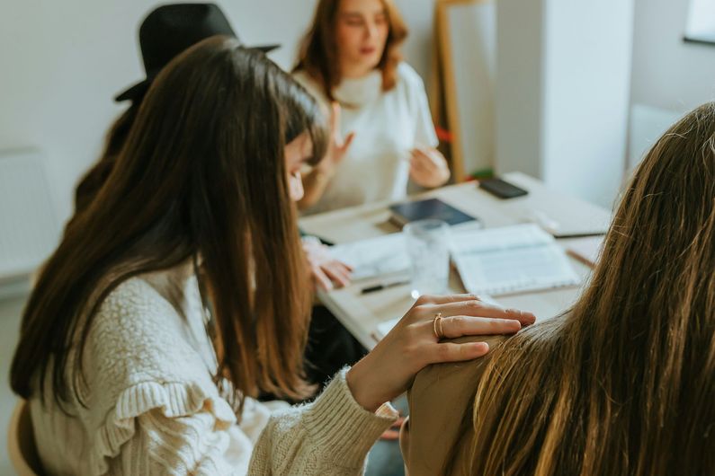 Group of people at a table, one person's hand on another's shoulder, discussing.