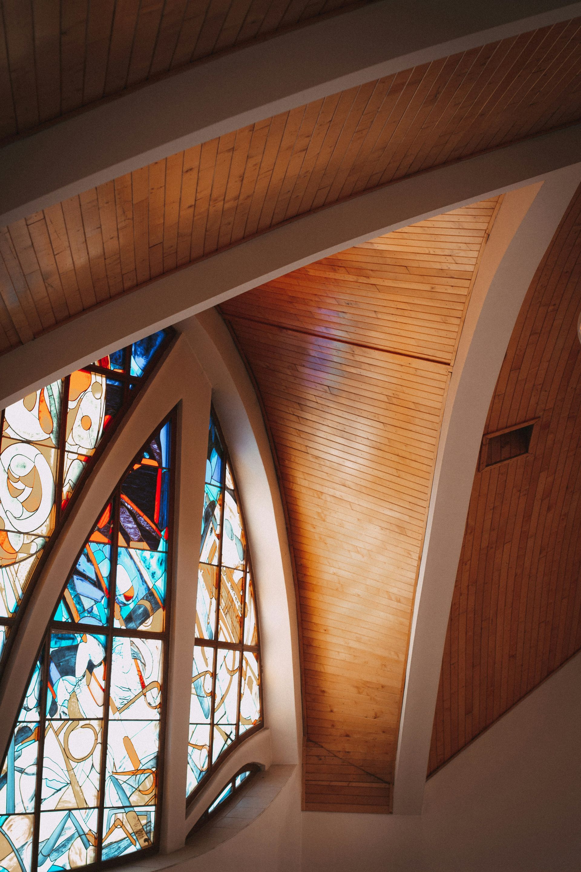 Arched wooden ceiling with stained glass window, illuminated by sunlight.