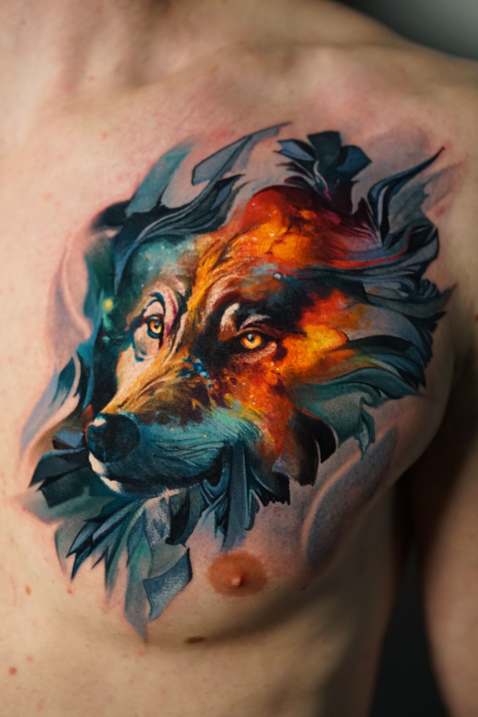 A man has a colorful tattoo of a wolf on his chest.