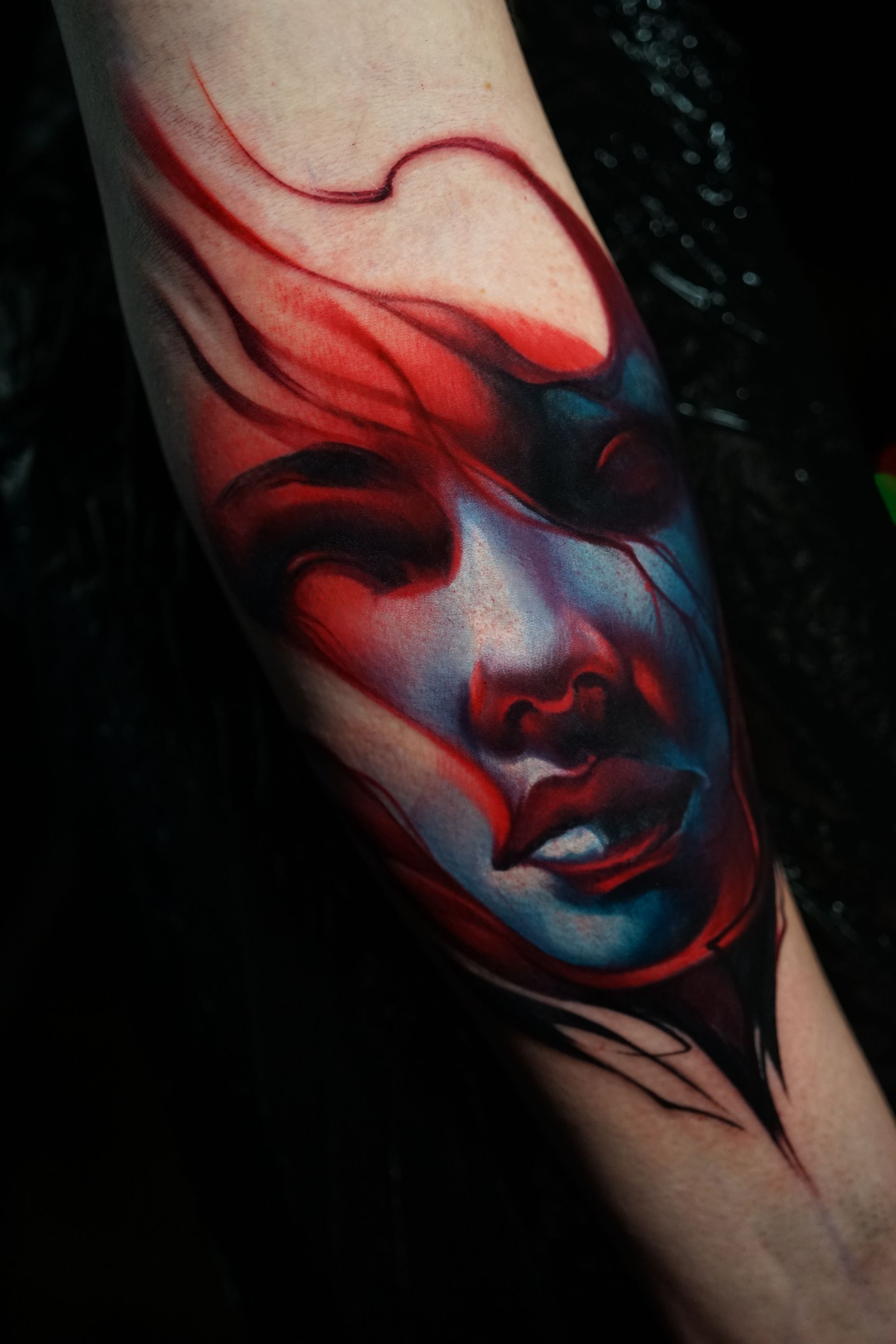 A person has a colorful tattoo of a woman 's face on their forearm.
