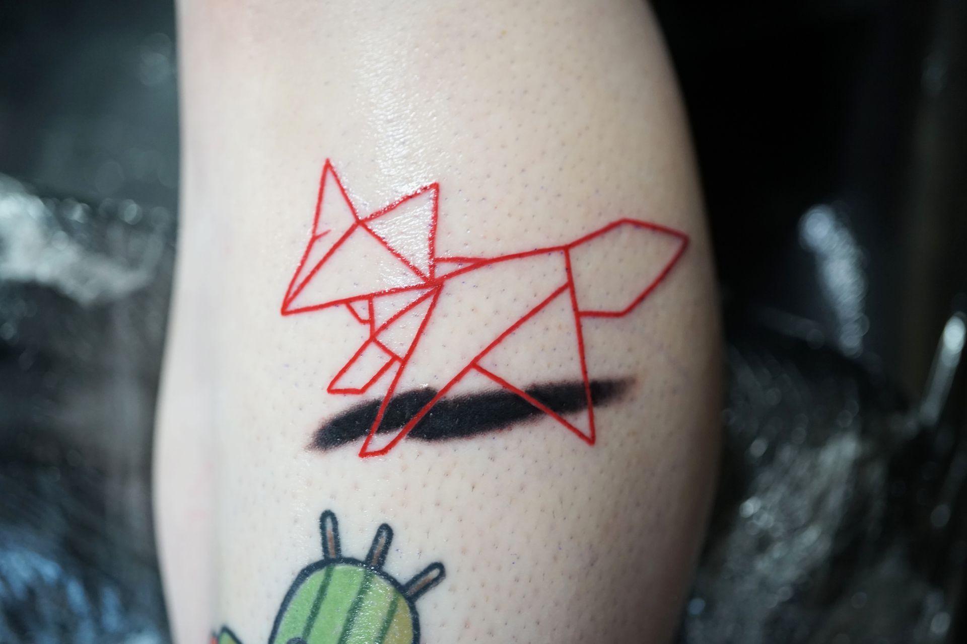 A person has a tattoo of a fox and a cactus on their leg.