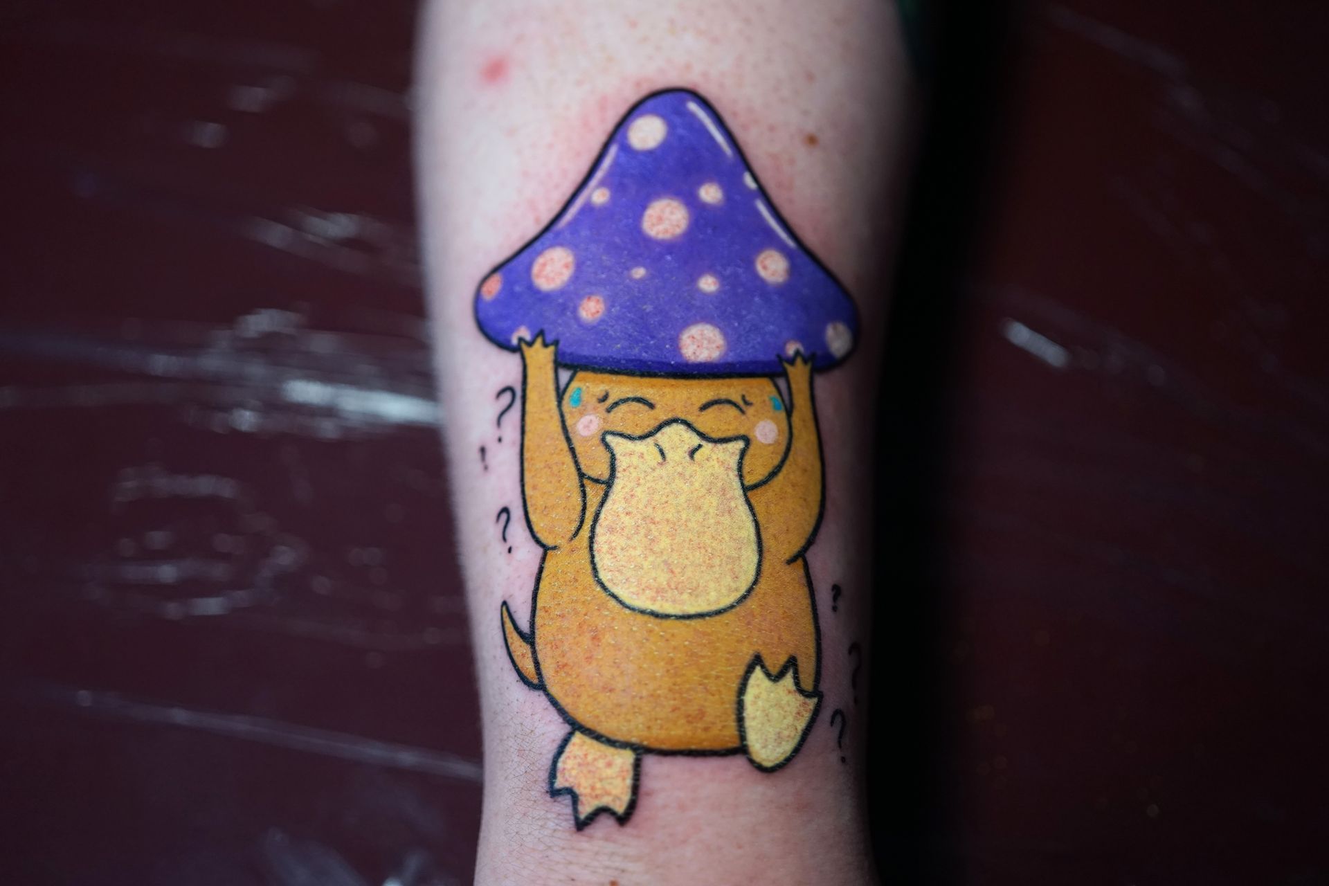 A person has a tattoo of a duck holding a mushroom on their leg.